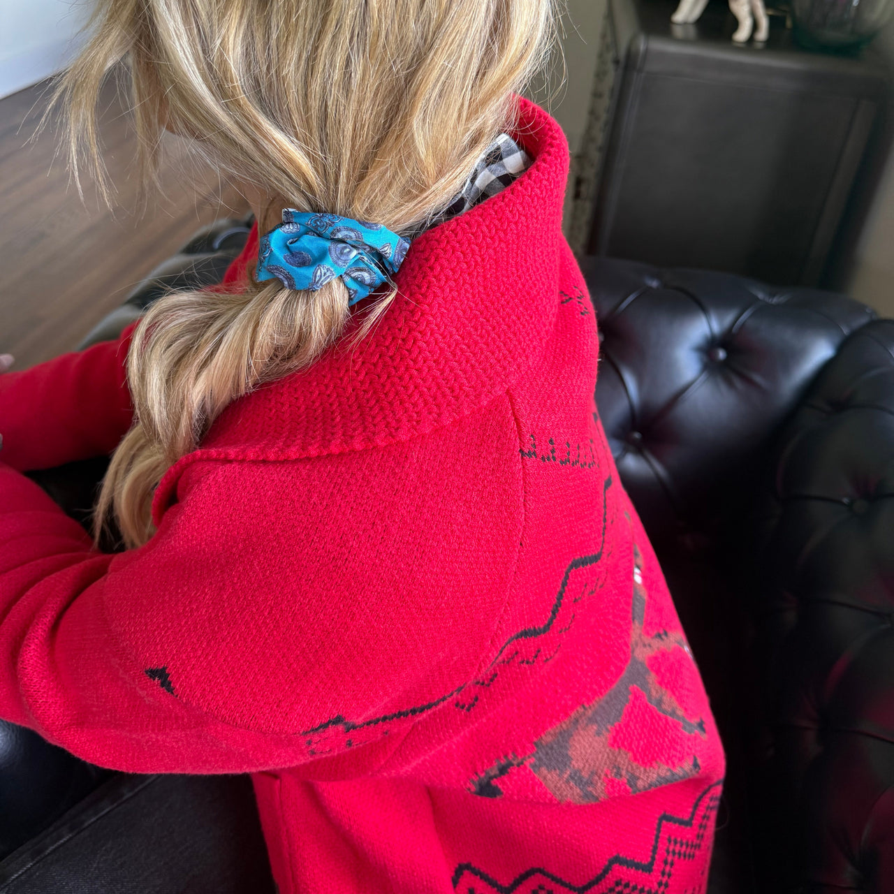 Person wearing a red hoodie with a blue scrunchie in their hair, sitting on a couch.